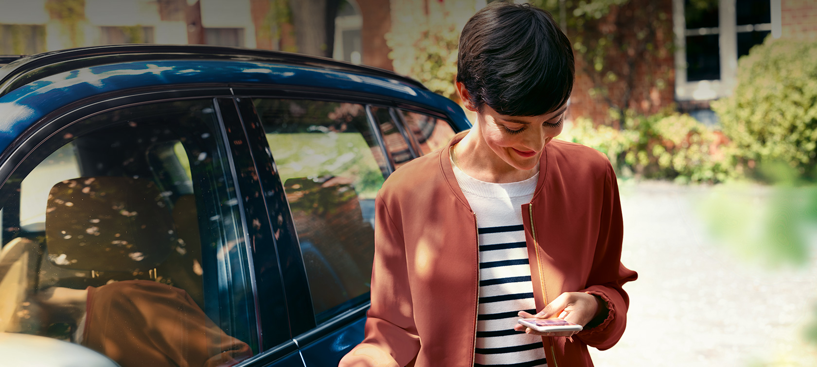 Služby BMW Teleservice, žena pred BMW hľadiaca na smartfón